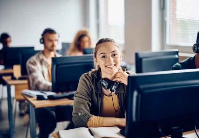 happy-female-student-using-desktop-pc-during-computer-class-and-looking-at-camera-.jpg